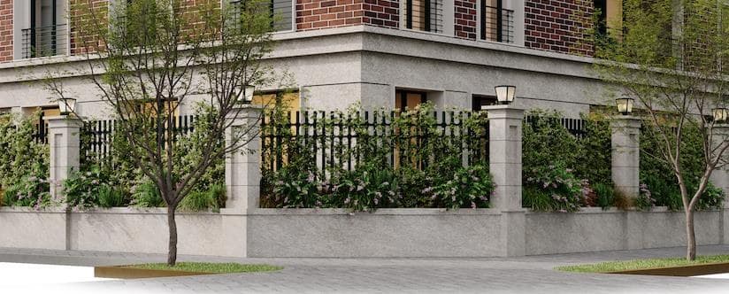 Cerco perimetral de piedra y reja de hierro, con jardineras corridas y árboles en la vereda